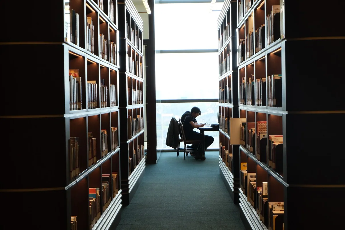 Ein Leser zwischen hohen Bücherregalen in einer Bibliothek.